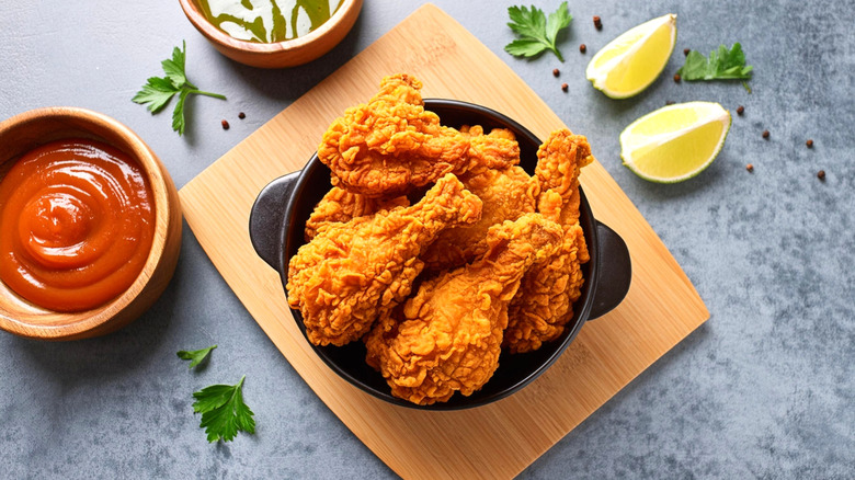 Bowl of fried chicken next to tomato sauce and limes