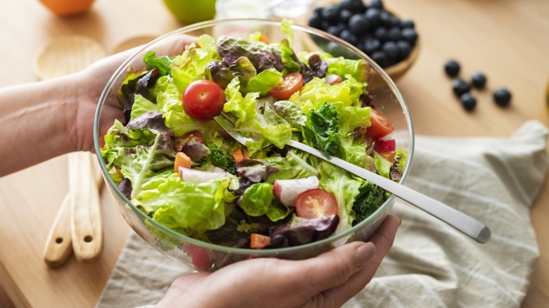 A person holding a big bowl of salad.