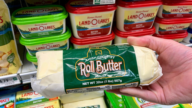 A hand holds a rolled package of Amish butter against brand name butters