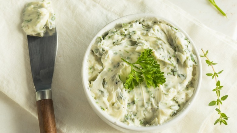 A ceramic bowl of butter infused with herbs with a knife next to it