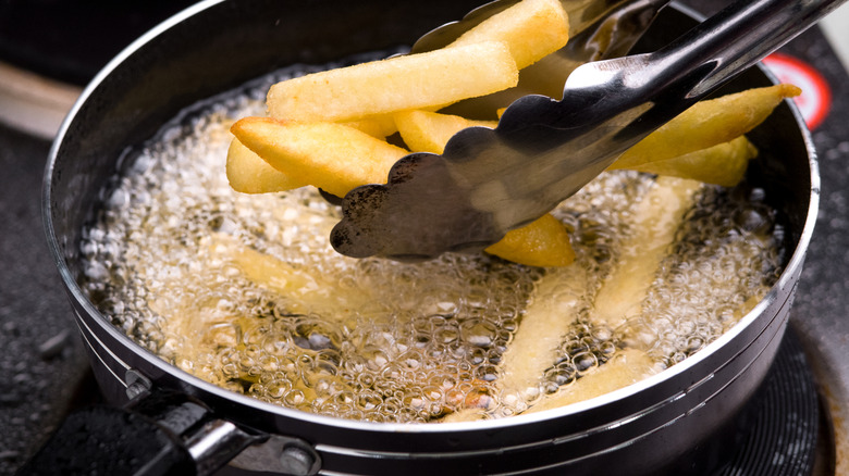 A person using tongs and cooking french fries in a pan of hot oil