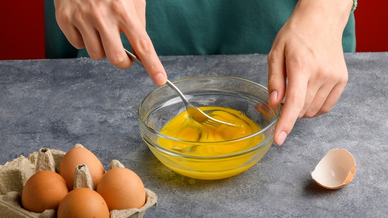 hands whip eggs with fork in glass bowl