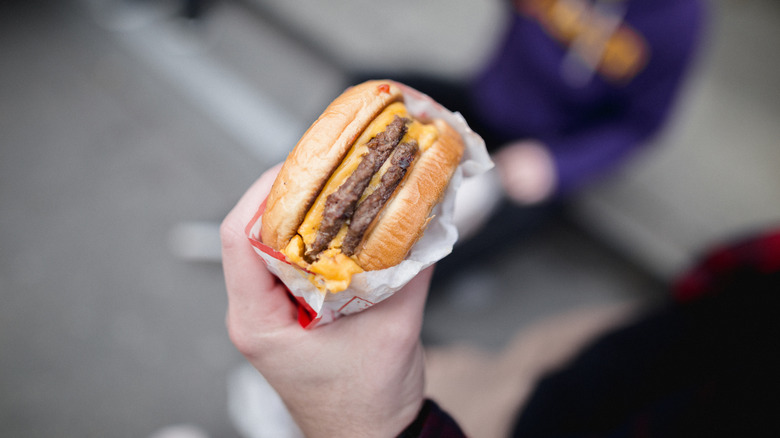 A person's hand holding a half-wrapped fast food burger