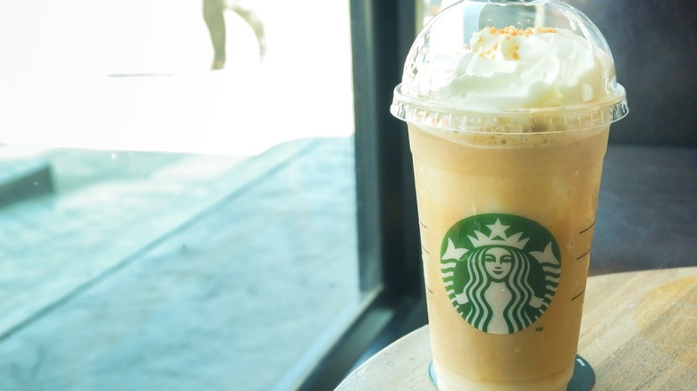 A Frappuccino from Starbucks on a wooden table near a window.