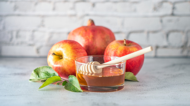 Apples and dish of honey on gray counter with leaves