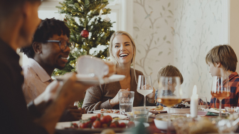 Adults and children gather at a dinner table with a Christmas tree in the background