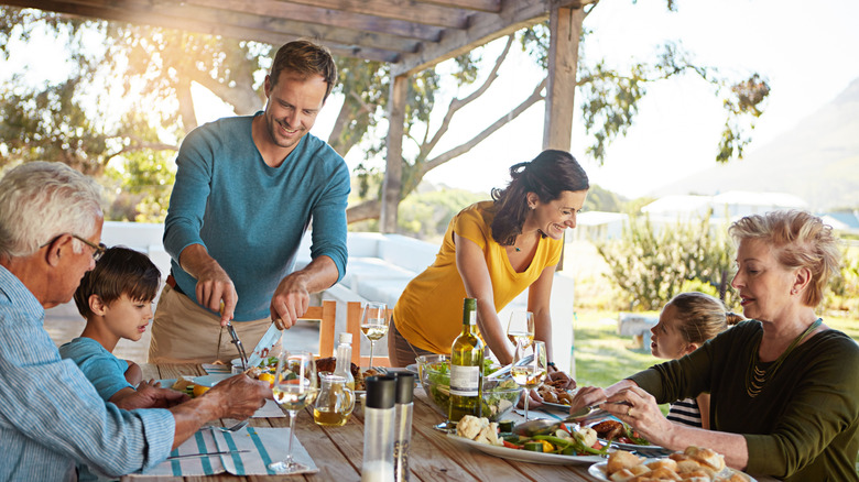 A multigenerational family eats at a table outdoors