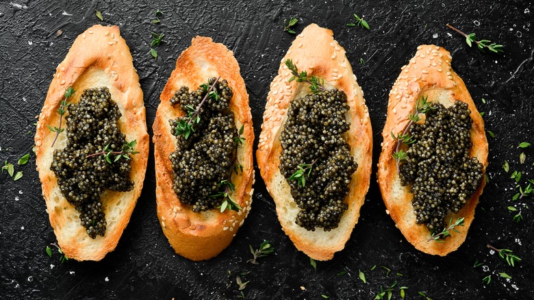 Caviar atop four small toast pieces on black background