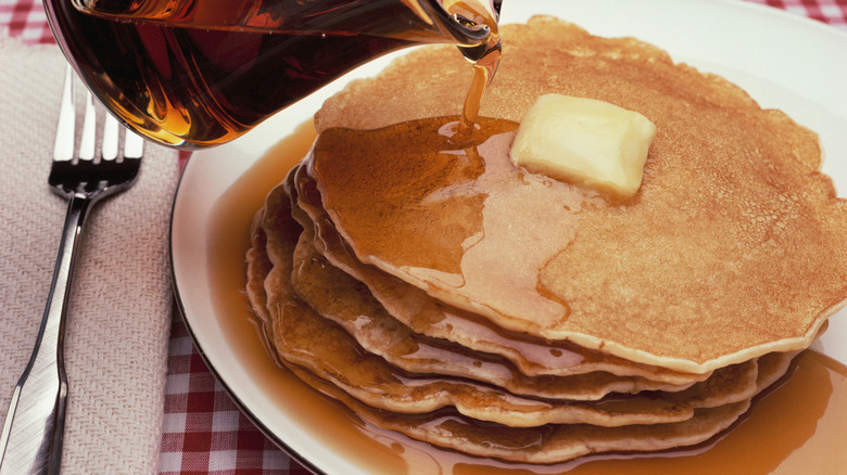 A stack of pancakes with a cube of butter and syrup on top