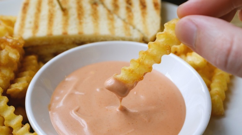 A crinkle-cut French fry being dipped into a pinkish sauce