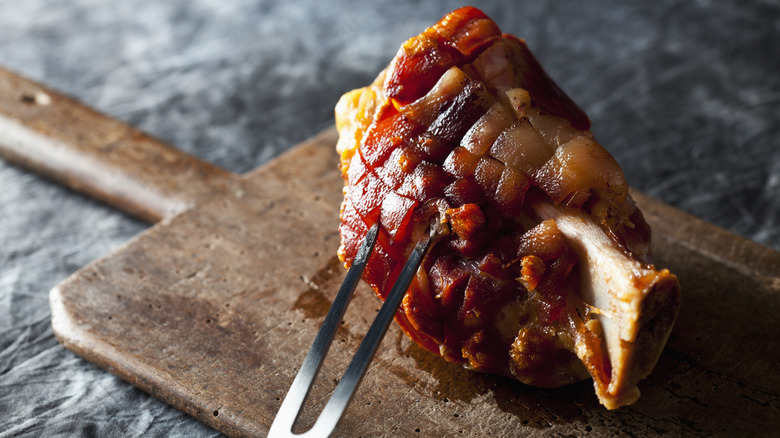 Ham hock on a wooden board with a carving fork