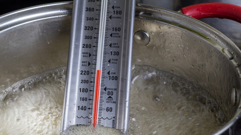 A candy thermometer inside a metal vat of boiling sugar