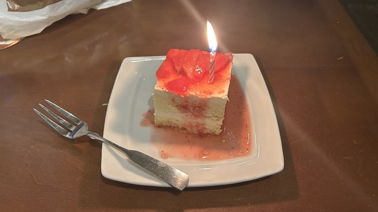 A piece of Olive Garden strawberry cake with a lit candle on top