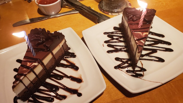 Two pieces of Olive Garden chocolate cake with lit candles