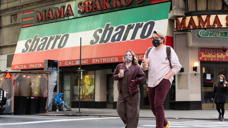 Two people cross a street outside a Sbarro location