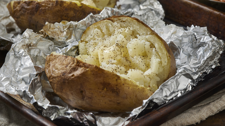 a baked potato in aluminum foil split open with black pepper