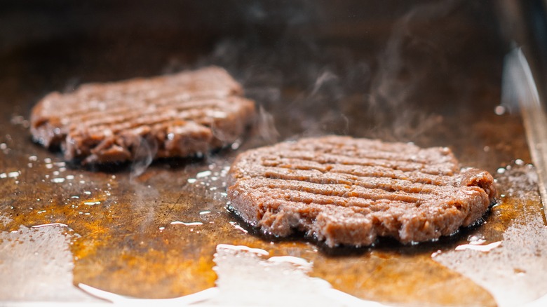 Two burger patties mashed on griddle