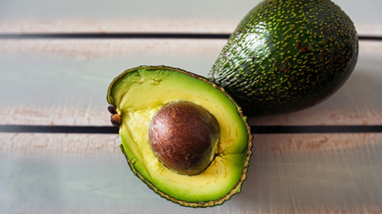 Split avocado on table next to whole avocado