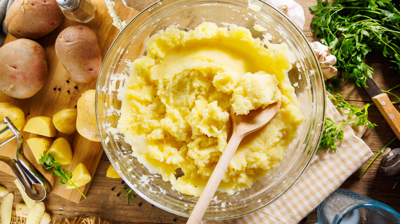 Mashed potatoes in bowl surrounded by raw whole potatoes