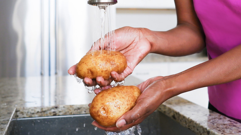 Person rinsing raw whole potatoes under running water