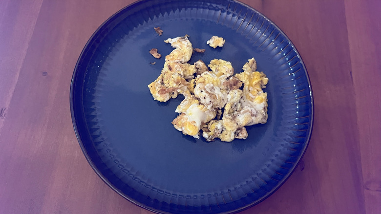 Eggs scrambled in bacon grease in a blue plate on a wooden table