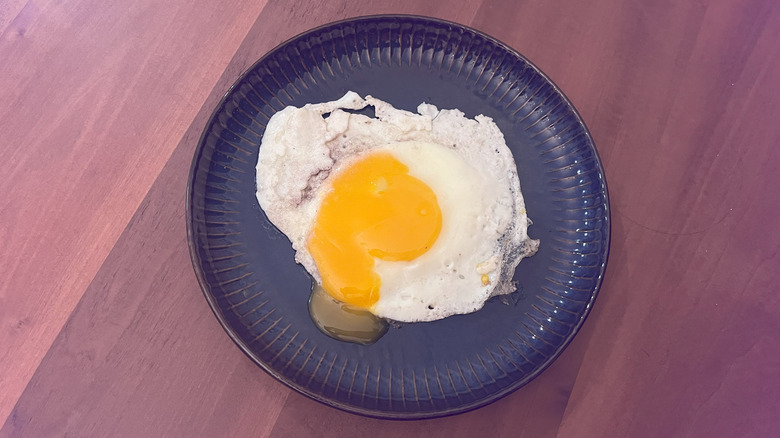 An egg fried in butter with a runny yolk on a blue plate, sitting on a wooden table