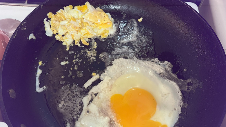 A scrambled egg and a fried egg share a frying pan on a stovetop