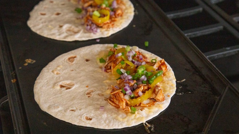 two flour tortillas with shredded cheese, chicken, and onions