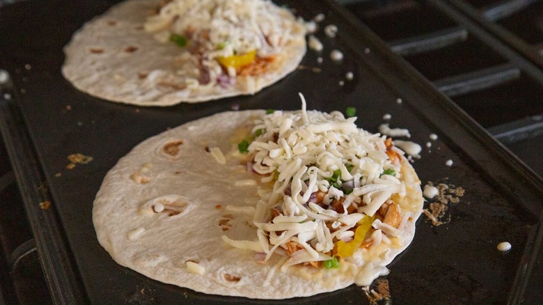 two flour tortillas with shredded cheese, chicken, and onions