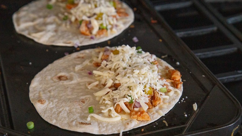 two flour tortillas with shredded cheese, chicken, and onions