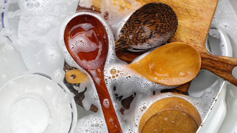 multiple wooden utensils soaking in soapy water with other dishes in kitchen sink