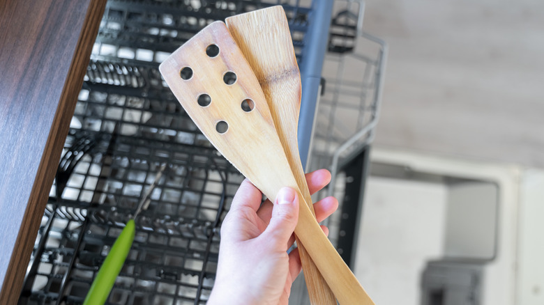 person holding two dry wooden spatulas over open dishwasher