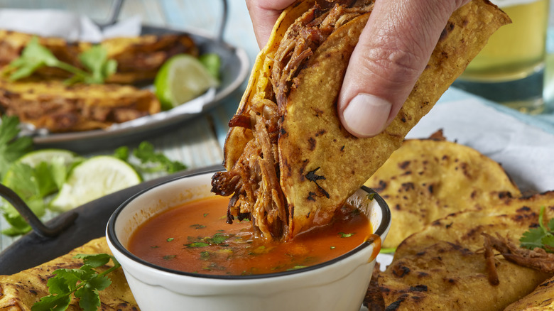 Fried birria tacos being dipped in sauce