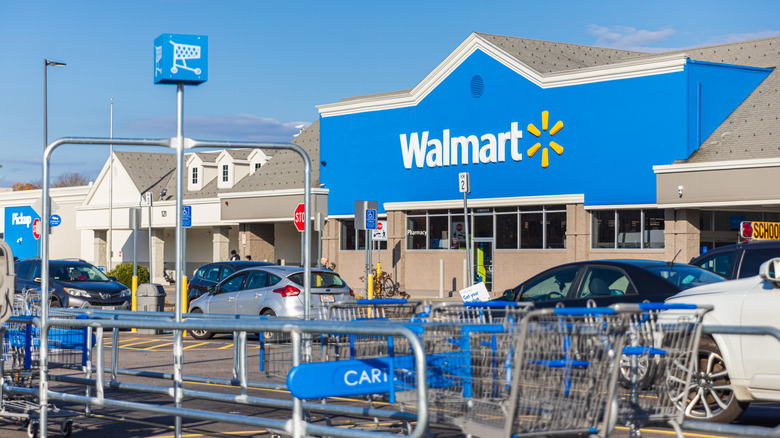 A blue Walmart store front with parked cars and shopping carts in the foreground