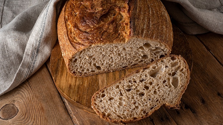 Sliced sourdough bread on a circular wooden board next to a cloth