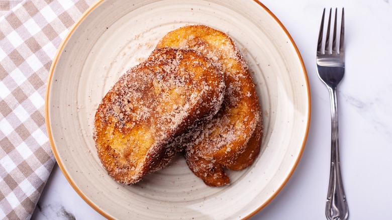 Sourdough French toast on a plate next to a fork and tablecloth