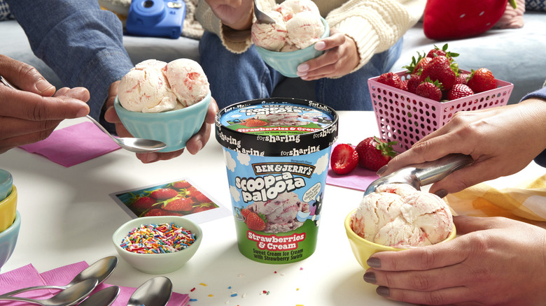 Close-up of Scoop-apalooza Strawberries & Cream pint on table surrounded by three consumers with bowls of ice cream flavor.