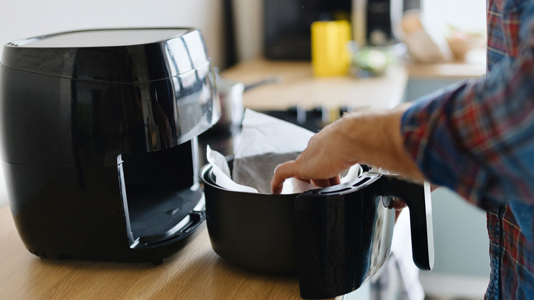 hands preparing an air fryer with parchment paper