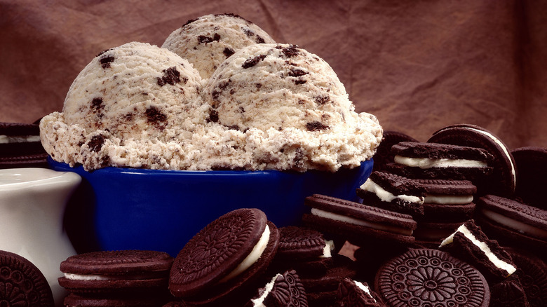 A bowl with three scoops of cookies and cream ice cream amid a pile of Oreo cookies