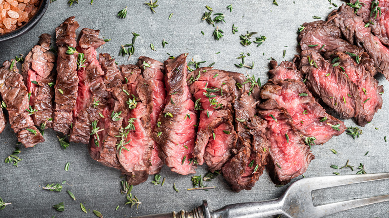 Several cut pieces of of strip steak with rosemary on a black surface