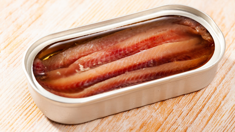 An open tin of anchovies on a wooden surface