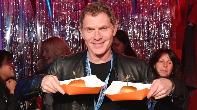 Bobby Flay holds two burgers in hand at event.