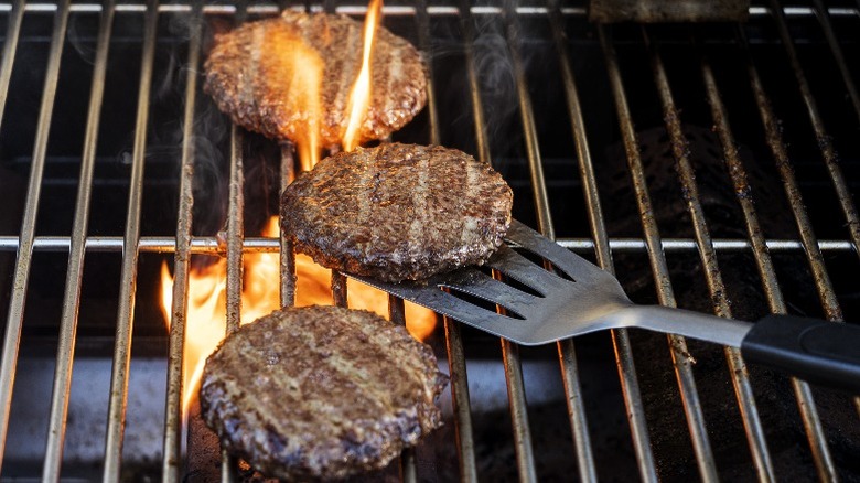 Three burgers on grill, the middle one is being flipped with a spatula.