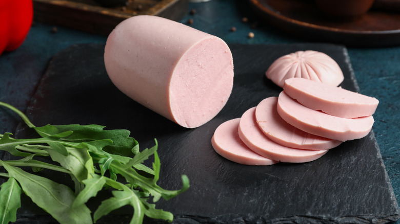 Sliced bologna lunch meat with arugula on a cutting board