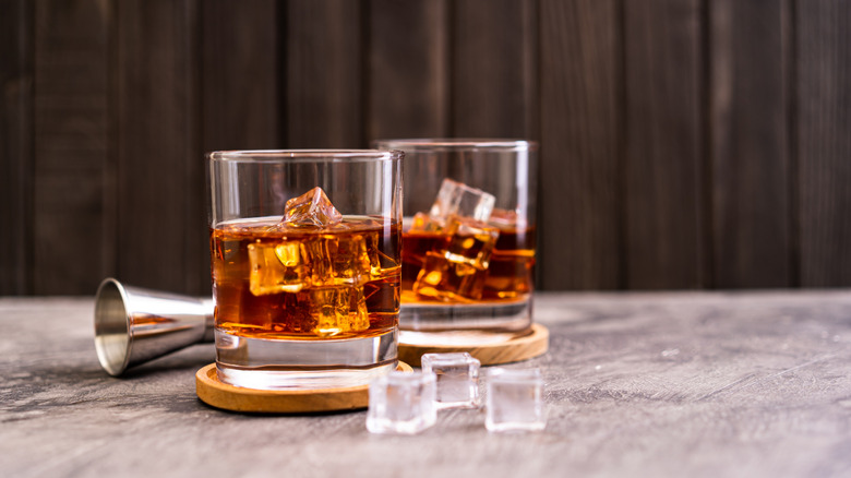 Two glasses of bourbon with ice sitting on cork coasters