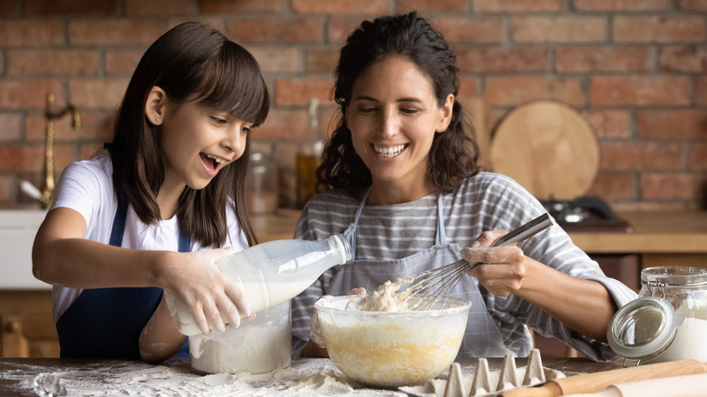 Parent and child adding milk to dough