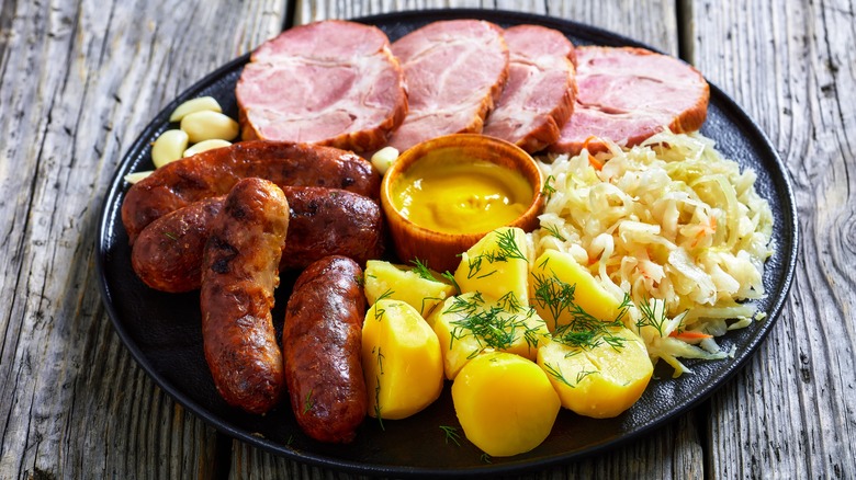 Bratwurst on plate with potatoes, sauerkraut, mustard and sliced pork