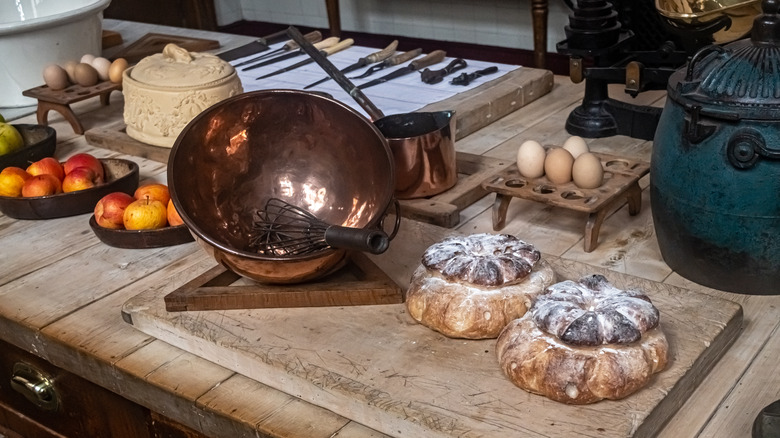 Victorian-style kitchen table with cooking tools, eggs, bread, and apples