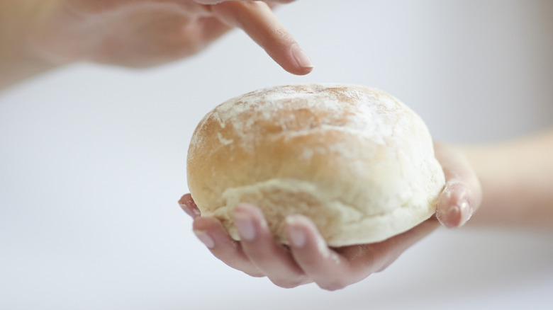 Hands holding a pale white bread roll