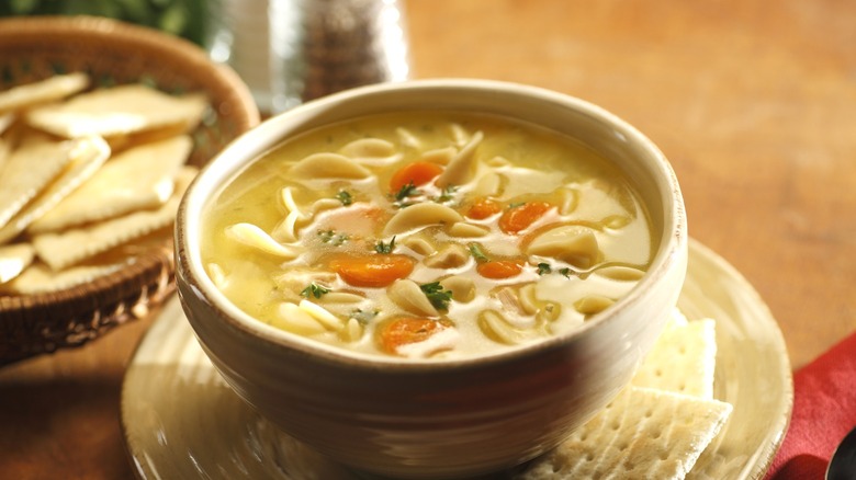 A bowl of chicken noodle soup being served with crackers